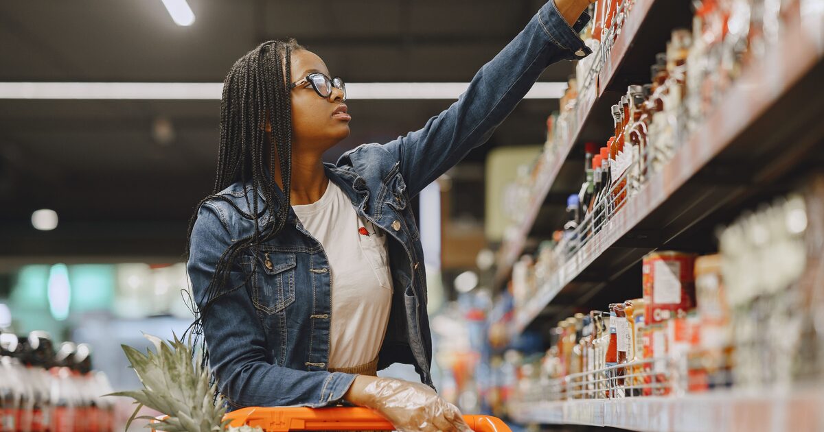 A shopper selecting a packaged product from a well-stocked supermarket shelf