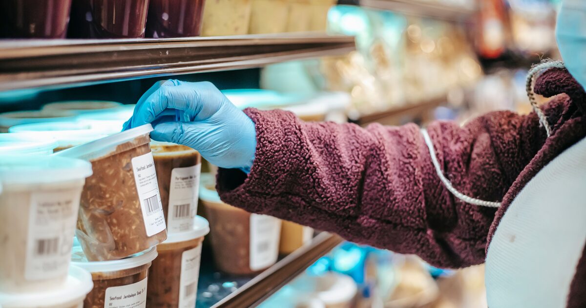 A shopper picking up a labelled deli container from a refrigerated store shelf
