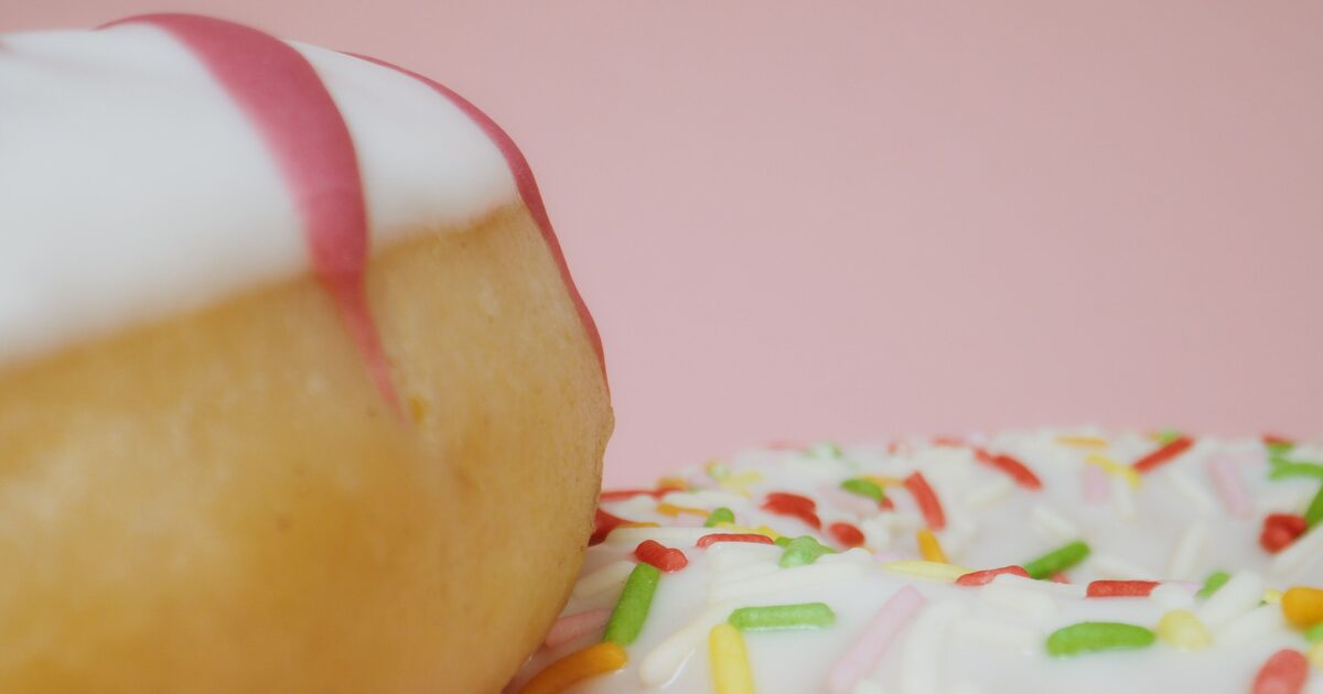 Two frosted donuts, one with white icing and one with colorful sprinkles, on a pink background