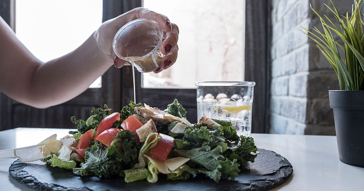 A hand pouring salad dressing over a fresh kale and tomato salad