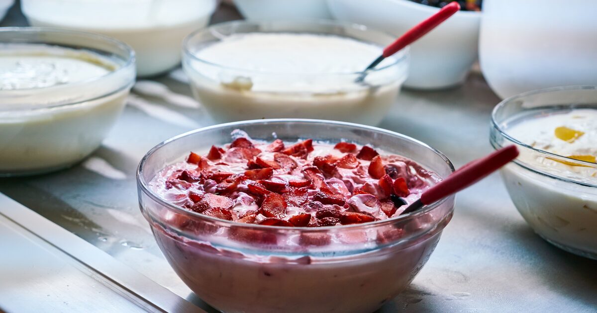 Glass bowls of plain and strawberry yogurt with spoons on a serving counter
