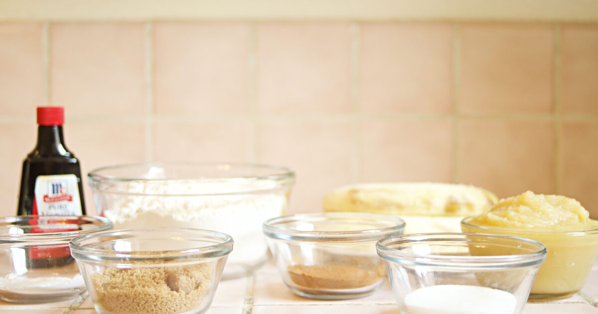 A bottle of pure vanilla extract beside bowls of baking ingredients on a kitchen counter