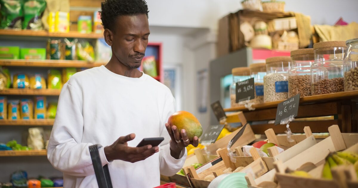 A shopper checking their phone while holding a piece of fruit in a grocery store